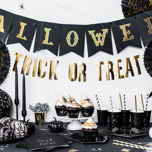 Black and gold halloween decorations, with trick or treat garland, cups, plates ahd napkins